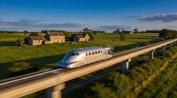 Fotografía de un Aérotrain plateado, aerodinámico, avanzando velozmente sobre una vía elevada de hormigón en la campiña francesa. Campos verdes y casas rurales al fondo.
