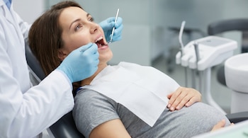 Primer plano de una mujer embarazada con cabello castaño en una silla dental, recibiendo tratamiento. Se ven las manos enguantadas del odontólogo con instrumentos.