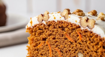 Primerísimo plano de un trozo de pastel de zanahoria con glaseado blanco y nueces. Se aprecian las fibras de zanahoria y la textura de la miga. Fondo desenfocado.