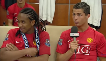Cristiano Ronaldo, con camiseta roja del Manchester United, sostiene un micrófono junto a Anderson Luis de Aberu Oliveira, quien sonríe con los brazos cruzados. Ambos llevan medallas