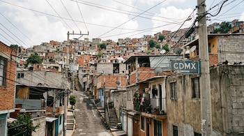 Casas de ladrillo y bloque en una calle empinada con postes de luz, un letrero azul con las letras C D M X y un enredo de cables.