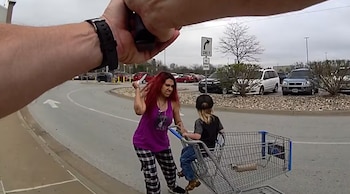 Desde la perspectiva de un oficial, una mujer de cabello rojo levanta un cuchillo cerca de un niño en un carrito de compras en un estacionamiento