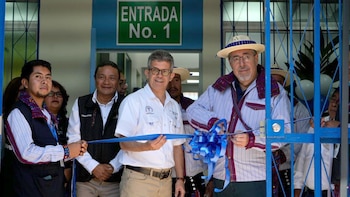 Grupo de hombres corta una cinta azul frente a una entrada de edificio con cartel "ENTRADA No. 1". El Presidente lleva sombrero de paja y camisa a rayas