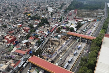 Vista aérea de un asentamiento urbano con una obra en construcción, autobuses en una avenida y un puente peatonal