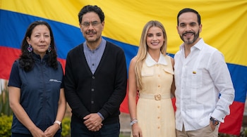 Cuatro personas, dos hombres y dos mujeres, posan sonrientes ante la bandera de Colombia. La mujer de la izquierda viste un chaleco oscuro con el logo JEP.