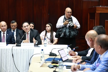 El Ministro de Gobernación de Guatemala, Marco Antonio Villeda, habla en un micrófono en una mesa de conferencias con otros funcionarios y un fotógrafo detrás