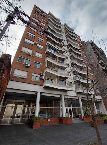 Un edificio alto con fachada de ladrillo, múltiples balcones y ventanas. En la planta baja hay una entrada acristalada y un garaje. Se ven postes y árboles sin hojas