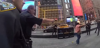Un oficial de policía apunta con un arma hacia una mujer en una calle iluminada por varias pantallas publicitarias