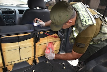 Oficial de Gendarmería Nacional con linterna y guantes blancos extrae un paquete envuelto en plástico rosa del interior de un asiento de auto desmantelado