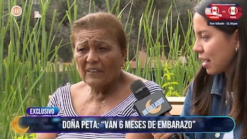 Una mujer mayor con camiseta a rayas habla frente a un micrófono sostenido por una reportera, sobre un fondo de plantas verdes