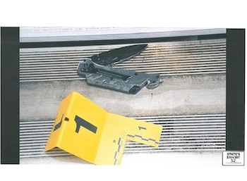 Una navaja de bolsillo abierta sobre escalones metálicos junto a un marcador numérico de evidencia de color amarillo con el número uno