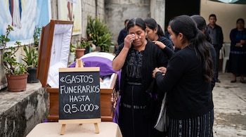 Una mujer se limpia las lágrimas al lado de un ataúd de madera y de un cartel con el texto Gastos funerarios hasta Q5.000.