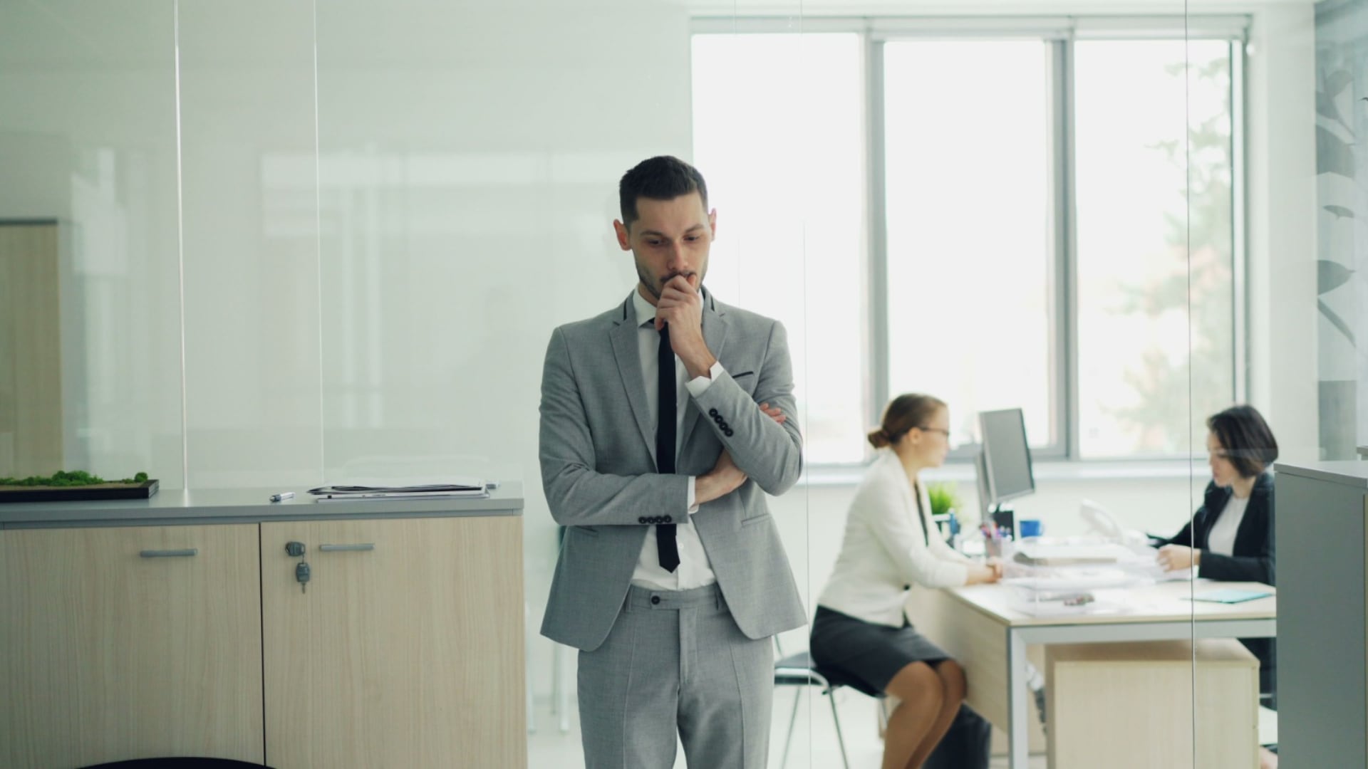 Un profesional evalúa sus opciones de carrera dentro de una oficina mientras dos compañeras de trabajo realizan sus labores al fondo. (Difusión)