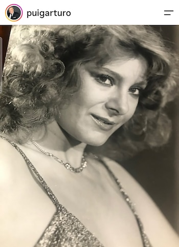 Retrato en blanco y negro de una mujer sonriente con cabello ondulado, collar fino y prenda de tirantes brillantes