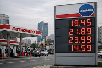 Un cartel digital rojo muestra precios elevados de combustible en una estación Petroperú en Lima, Perú, con el logo de OSINERGMIN. Se ven autos y edificios al fondo.