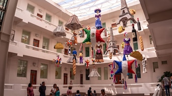 Piñatas con forma de la Torre Eiffel, pirámides y estrellas con las banderas de México y Francia cuelgan en el patio de un edificio.
