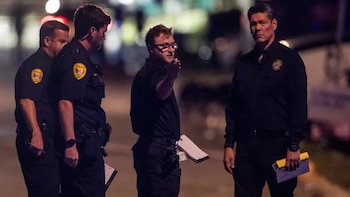 Cuatro oficiales de policía vestidos con uniformes oscuros permanecen de noche en una calle mientras sostienen carpetas y documentos