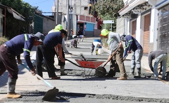 Vista de varios obreros en ropa de trabajo y sombreros, usando palas y carretillas para verter y esparcir concreto fresco en una calle