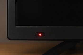 Detalle del marco inferior de un televisor con la pantalla negra y una pequeña luz LED roja encendida.