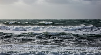 Vista frontal del mar con olas grandes y espumosas bajo un cielo nublado y gris. El agua verde oscura muestra crestas blancas y rociadas por el viento.