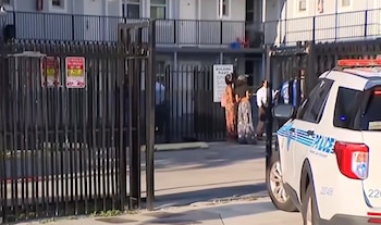 Un vehículo policial estacionado junto a la reja de entrada de un edificio residencial con varias personas en el patio