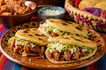 Tres gorditas de maíz rellenas con chicharrón, lechuga picada y queso sobre un plato de barro con adornos verdes.
