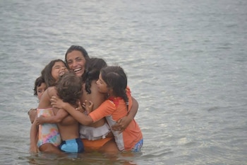 Una mujer y varios niños se abrazan dentro del agua con trajes de baño