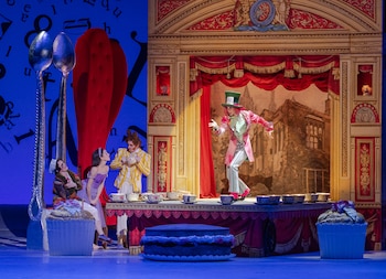 Cuatro actores en disfraces sobre un escenario con decorado teatral, que incluye una mesa con tazas, cucharas gigantes, dos cupcakes grandes y una torta