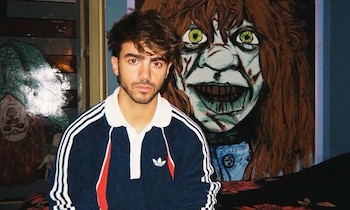 Fede Vigevani, joven, viste camiseta deportiva azul con rayas blancas; de fondo, dos pinturas de rostros de terror, uno de ellos invertido