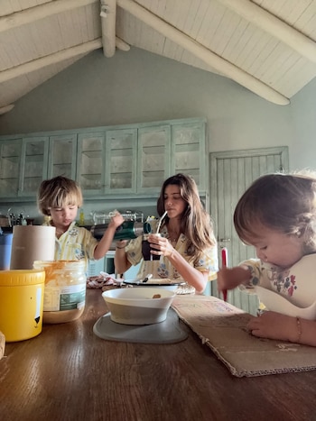 Calu Rivero vierte agua caliente en un mate mientras sus hijos pequeños, Tae y Bee, están sentados a una mesa de madera clara con comida