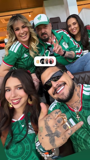 Cinco personas, dos en primer plano y tres en segundo, visten camisetas verdes de la selección mexicana; un hombre con gafas de sol y tatuajes hace un pulgar arriba