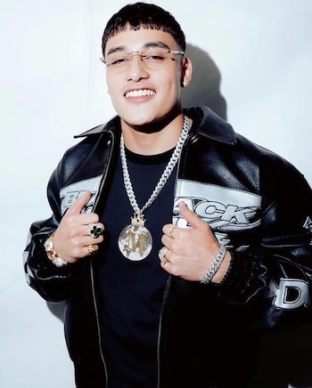 Un hombre con gafas y chaqueta de cuero negra posa sonriente luciendo cadenas al cuello y anillos en las manos