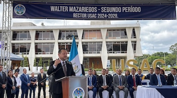 Walter Mazariegos habla en un podio con micrófono, bandera de Guatemala y personas sentadas. Un banner azul detrás dice "Walter Mazariegos - Rector USAC".