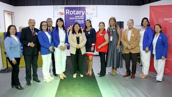 Grupo de once personas, seis mujeres y cinco hombres, de pie posando frente a pancartas de Rotary Club Lima Gente de Acción y Asociación Benéfica Amarán