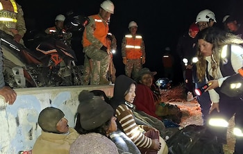 Un grupo de personas sentadas en la oscuridad mientras personal de rescate con chalecos reflectantes y linternas les asisten