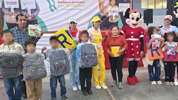 Un grupo de adultos y niños sostiene mochilas, juguetes, letras grandes y una gorra con la palabra POLICIA, frente a un banner de Inabif