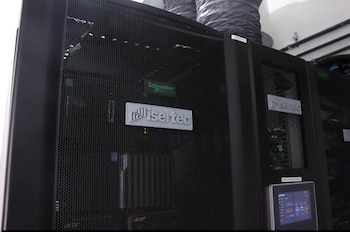 Tres racks de servidores negros con rejilla, logos de Isertec, Schneider Electric y Acer, una pantalla con datos y conductos de ventilación