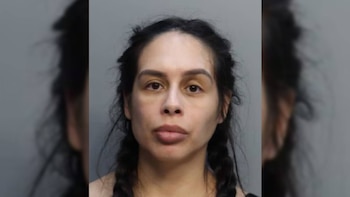 Una mujer con cabello oscuro trenzado, ojos marrones y boca cerrada. Viste ropa oscura y está frente a un fondo gris claro
