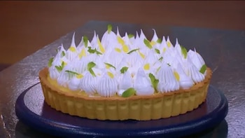 Tarta con base de masa, relleno y picos de merengue blanco decorados con ralladura verde, servida sobre un plato azul oscuro