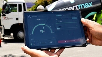 Primer plano de manos sosteniendo una tableta con una aplicación de monitoreo de concreto. Se ve un camión mezclador de cemento al fondo