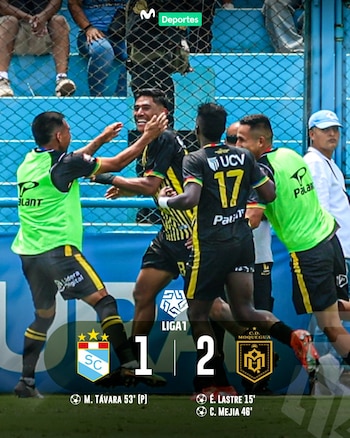 Jogadores do time de futebol com camisetas pretas e amarelas comemoram um gol ou vitória em campo, com uma cerca azul ao fundo.