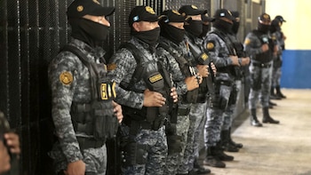 Grupo de agentes de seguridad con uniformes camuflados, chalecos tácticos negros, pasamontañas y gorras, de pie en fila en un centro de aislamiento