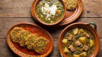 Primer plano de tres platillos mexicanos con huauzontle en recipientes de barro. Incluye una sopa, tortitas en salsa roja y un guiso con carne y papas.