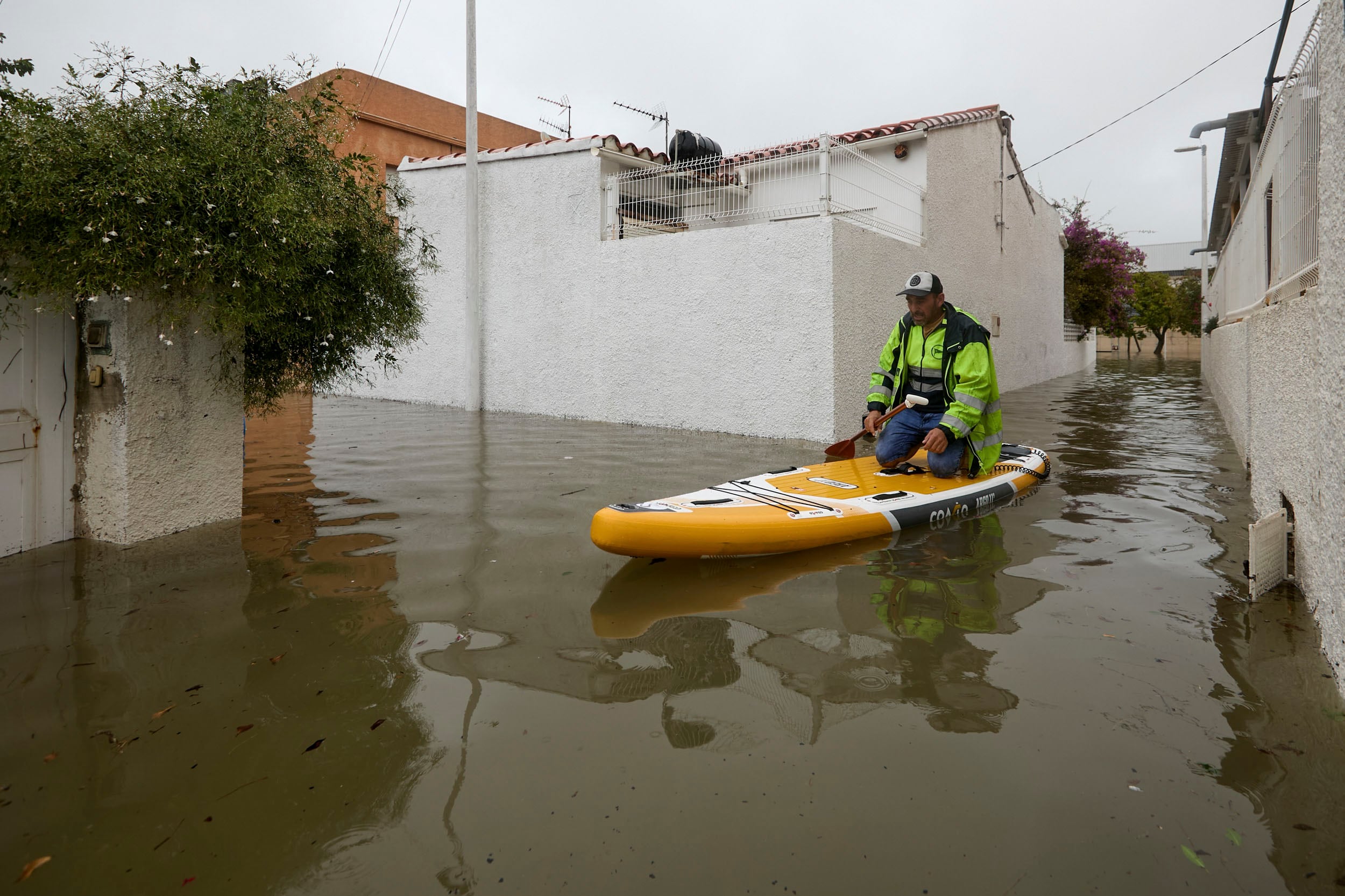 Un hombre se desplaza sobre una tabla de surf en la zona residencial próxima a la playa de Venecia, en el Grao de Gandía. (Natxo Francés/EFE)