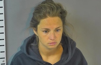 Mujer caucásica con cabello castaño claro recogido y sudadera oscura mirando al frente, con ojos azules. Medidor de altura visible a la izquierda sobre fondo gris