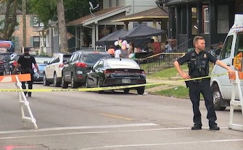 Dois policiais uniformizados patrulham uma rua coberta com fita amarela em Toledo, Ohio, com carros e prédios ao fundo.