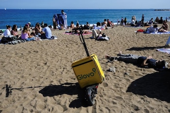 Una mochila de entrega de alimentos de Glovo sobre un patinete eléctrico mientras un repartidor descansa cerca. (REUTERS/Nacho Doce)