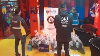 Agentes con chalecos de la Policía Judicial y de Lotería de la Ciudad observan bolsas con pertenencias incautadas en un local