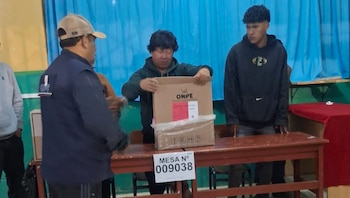 Três homens numa sala montaram uma assembleia de voto. Um segura uma caixa com a logomarca do ONPE, enquanto o outro observa. Vendo sinais de