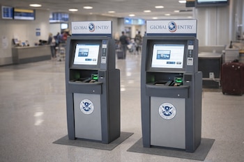 Dos kioscos grises de Global Entry con pantallas táctiles y el logo de Aduanas y Protección Fronteriza, situados en un aeropuerto con un piso claro.